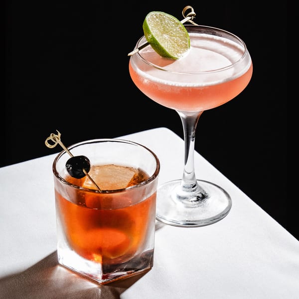Two Romesco Mexiterranean Bistro cocktails: an Old Fashioned and a pink drink with a lime.