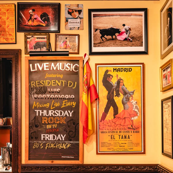 A wall adorned with framed bullfighting posters, a Spanish flag, and a chalkboard advertising live music.