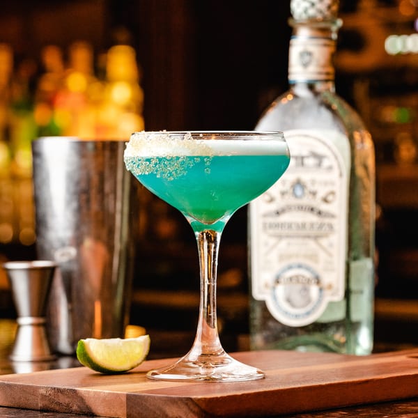 A vibrant blue cocktail with a sugared rim and lime wedge on a wooden bar top.