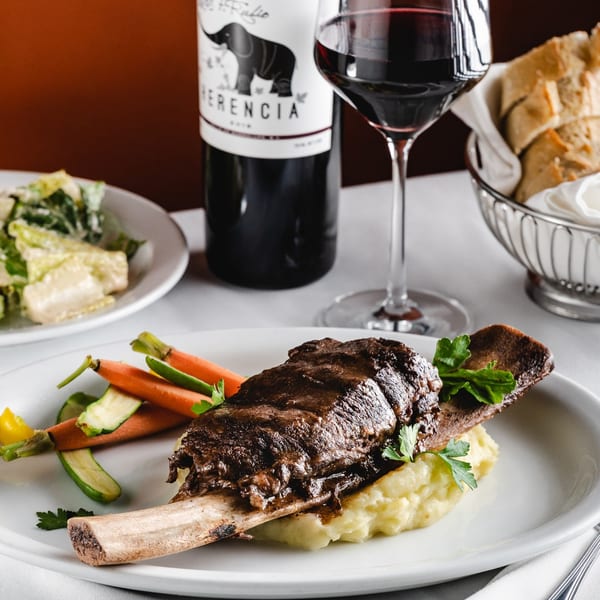 Braised short rib with mashed potatoes, carrots, and zucchini, alongside wine and salad.