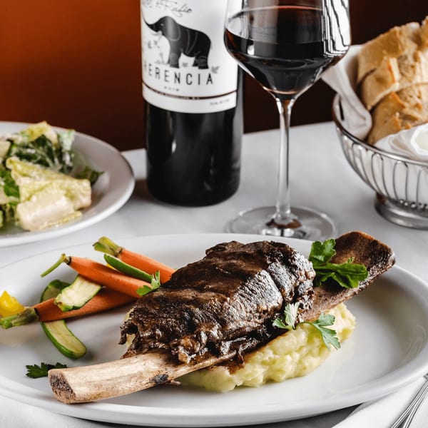 Braised short rib on mashed potatoes with carrots, zucchini, and a glass of red wine.