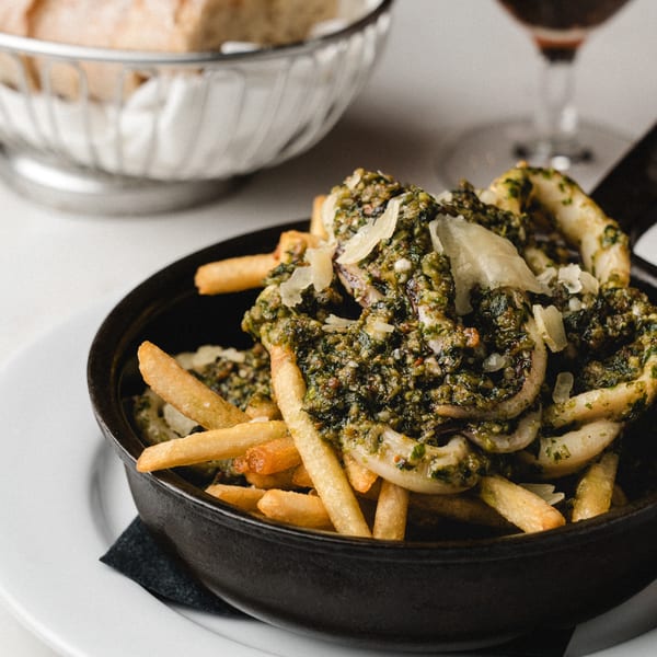 Calamari and french fries topped with green pesto and parmesan cheese in a black bowl.