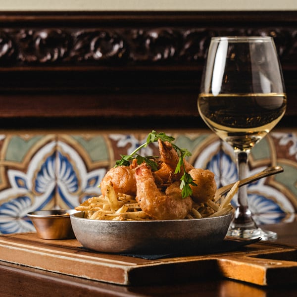 Fried shrimp and french fries in a metal bowl with a glass of white wine.