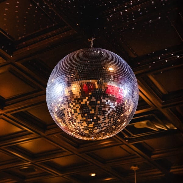 A large, shimmering disco ball hangs from a dark, patterned ceiling, reflecting warm light.