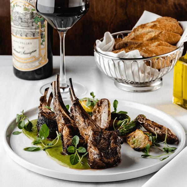 Grilled lamb chops with green sauce and roasted vegetables, served with red wine and bread.