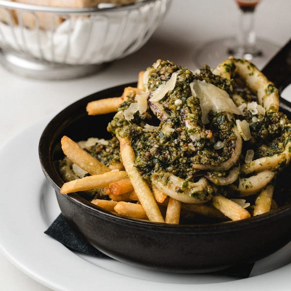 Romesco Mexiterranean Bistro's fries and calamari topped with pesto and parmesan in a black skillet.