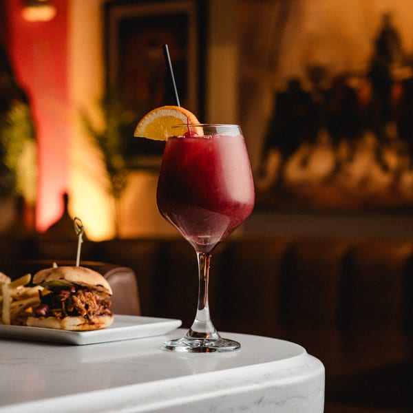 A Romesco Mexiterranean Bistro sangria with an orange slice and a slider on a white table.