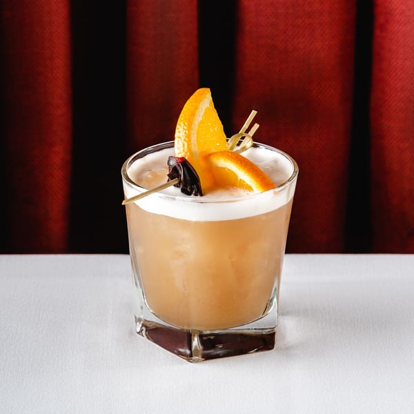 Romesco Mexiterranean Bistro cocktail with orange slices and a dark garnish on a white tablecloth.