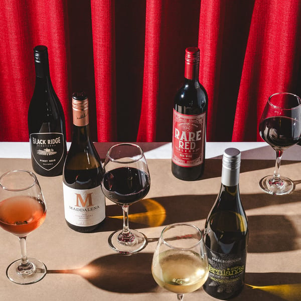 Various wine bottles and glasses with red, rosé, and white wine against a red curtain.